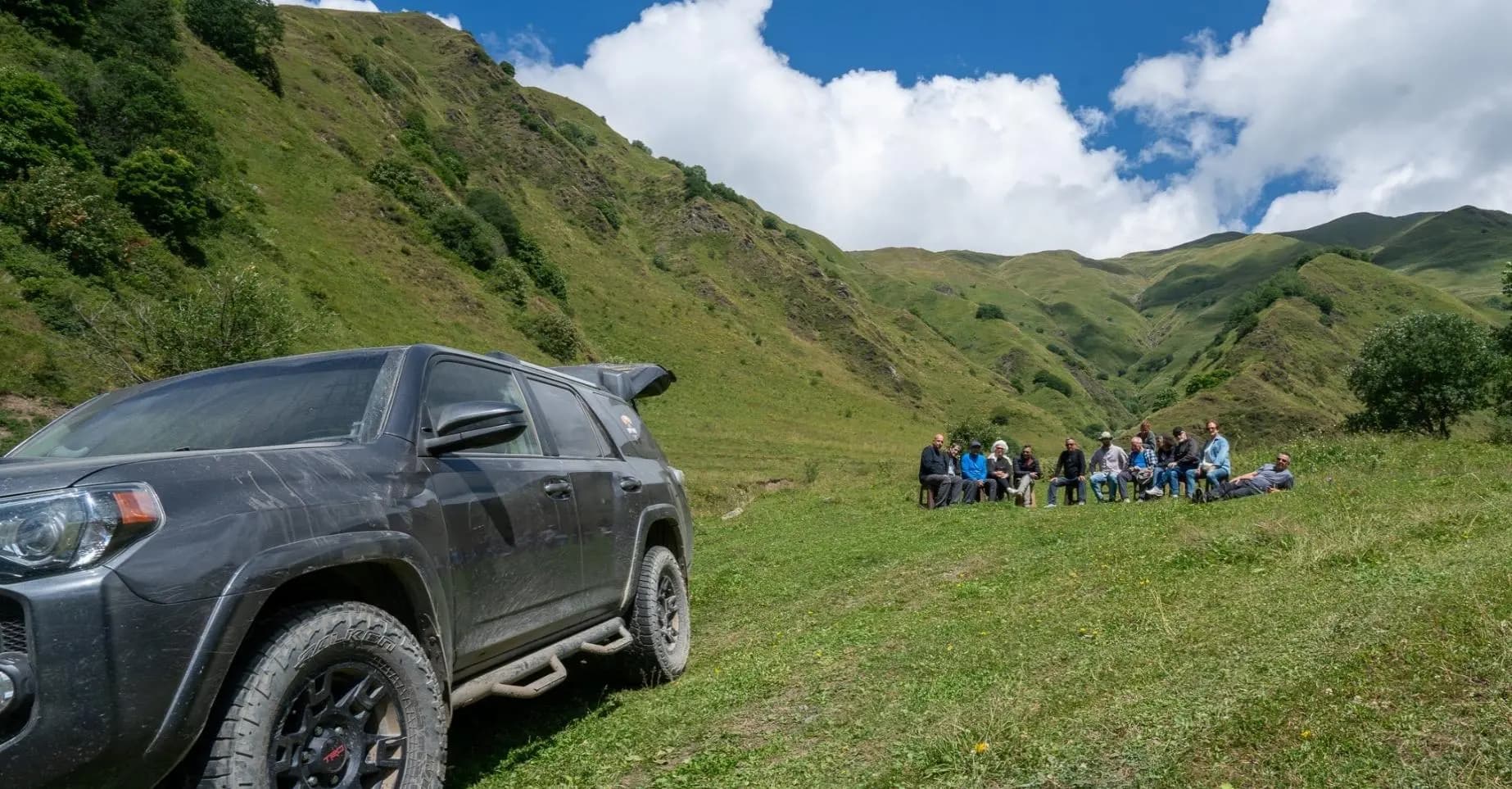 4WD vehicle beside a small travel group in the Georgian mountains